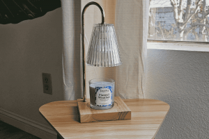 Flannel Weather Soy Candle Under A Stylish Lamp On A Wooden Table