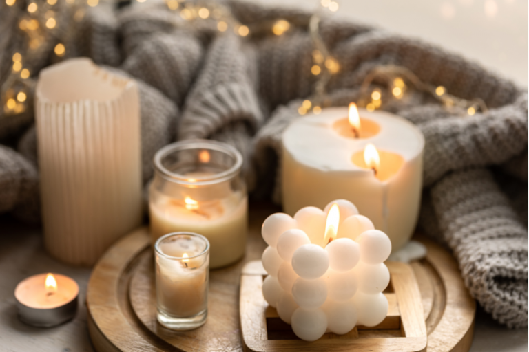 Candle Decor Ideas Displayed With A Cozy Arrangement Of White Candles In Various Shapes, Including A Bubble Candle And Jar Candles, Styled On Wooden Trays With Soft Knit Blankets And Fairy Lights.