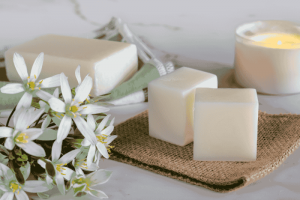 blog 1 A Cozy And Eco-Friendly Home Setup Featuring Natural Soy Wax Melts, A Lit Candle, And Fresh White Flowers On A Soft Fabric Surface.